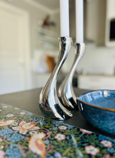 Två silvriga George Gensen ljusstakar med ljus, en blå skål och en Morris bordstablett.