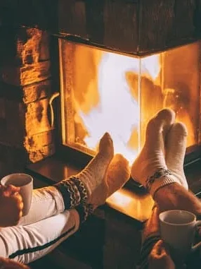 Fötter i strumpor framför en öppen eld med muggar i handen.