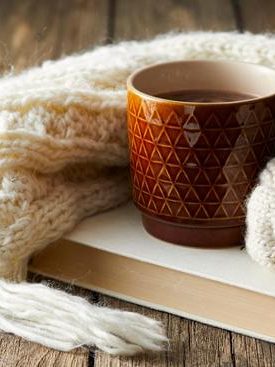 En mugg i terrakotta med en randig scarf och en öppen bok på ett träbord.