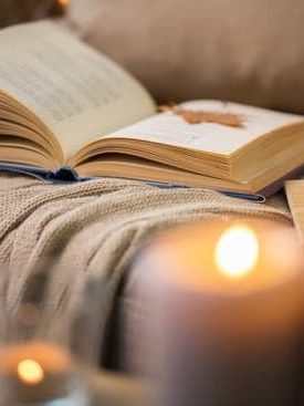 Öppen bok på en mjuk filt med ljus i bakgrunden.